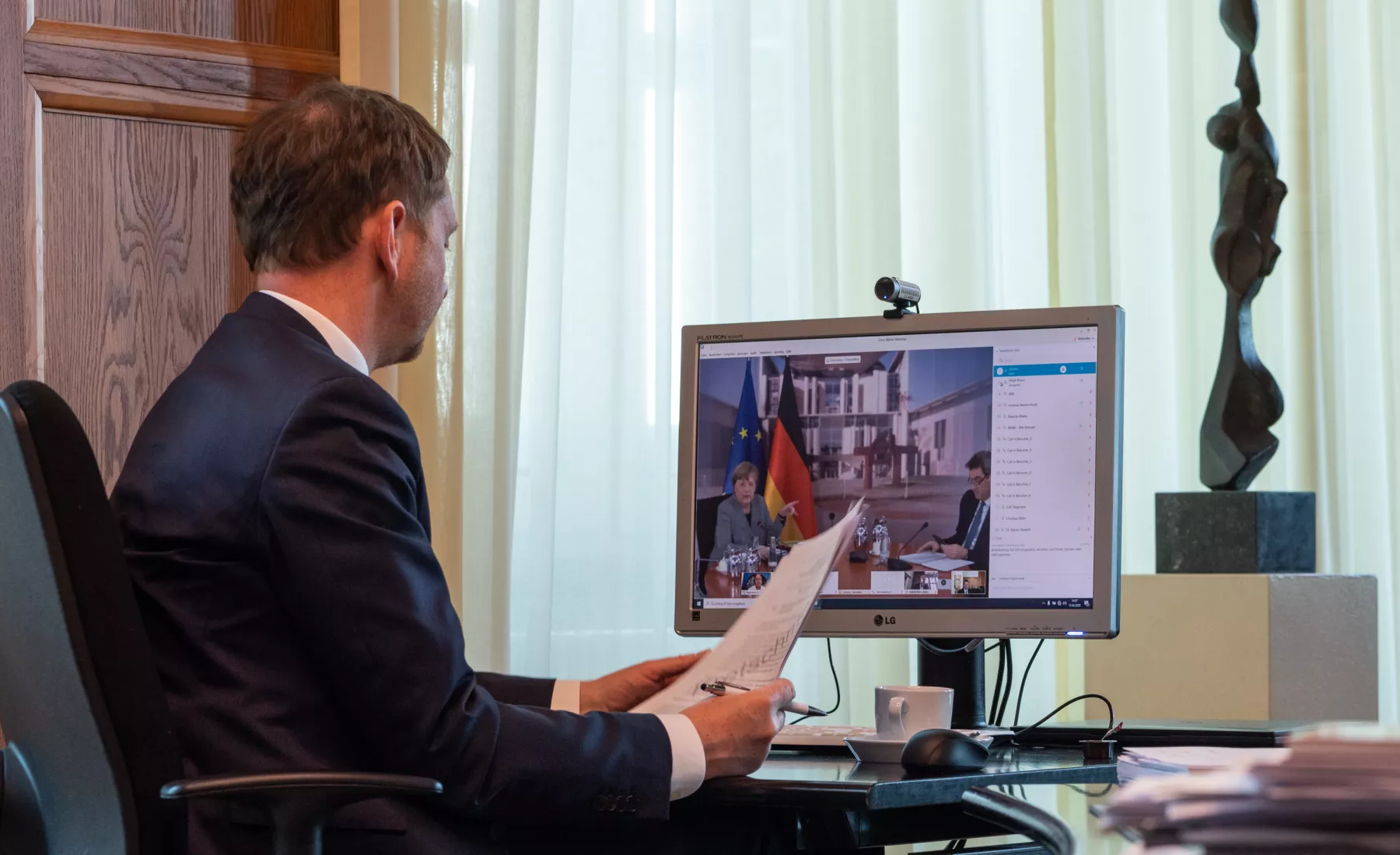 Michael Kretschmer (CDU), Ministerpräsident von Sachsen, sitzt in einem Büro in der Staatskanzlei vor einem Computerbildschirm und spricht während einer Schaltkonferenz per Video mit Bundeskanzlerin Angela Merkel (CDU, l.) und Markus Söder (CSU), Minister