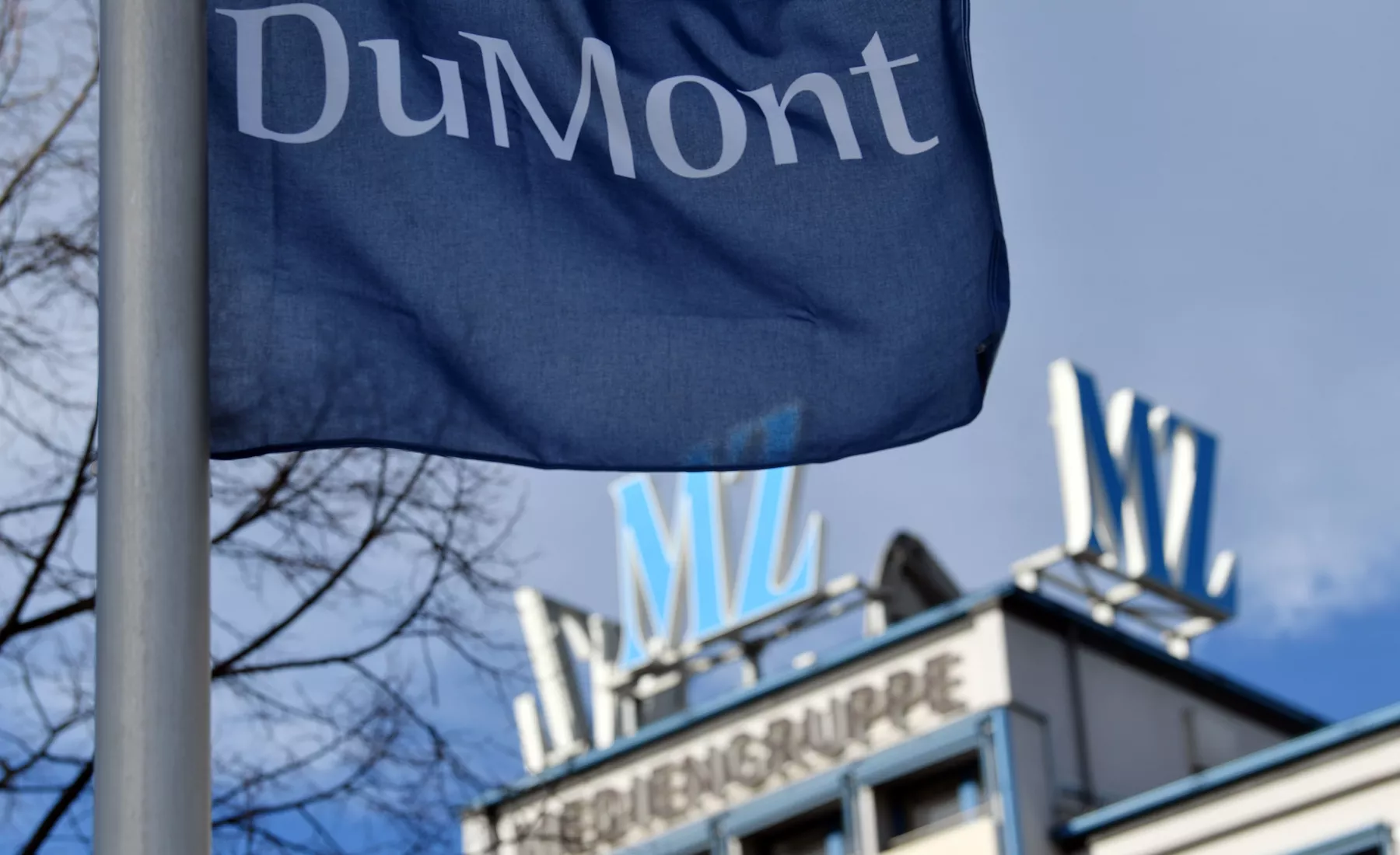 Eine Fahne mit dem Schriftzug des Medienhaus DuMont weht vor dem Hauptgebäude der Mediengruppe Mitteldeutsche Zeitung in Halle/Saale