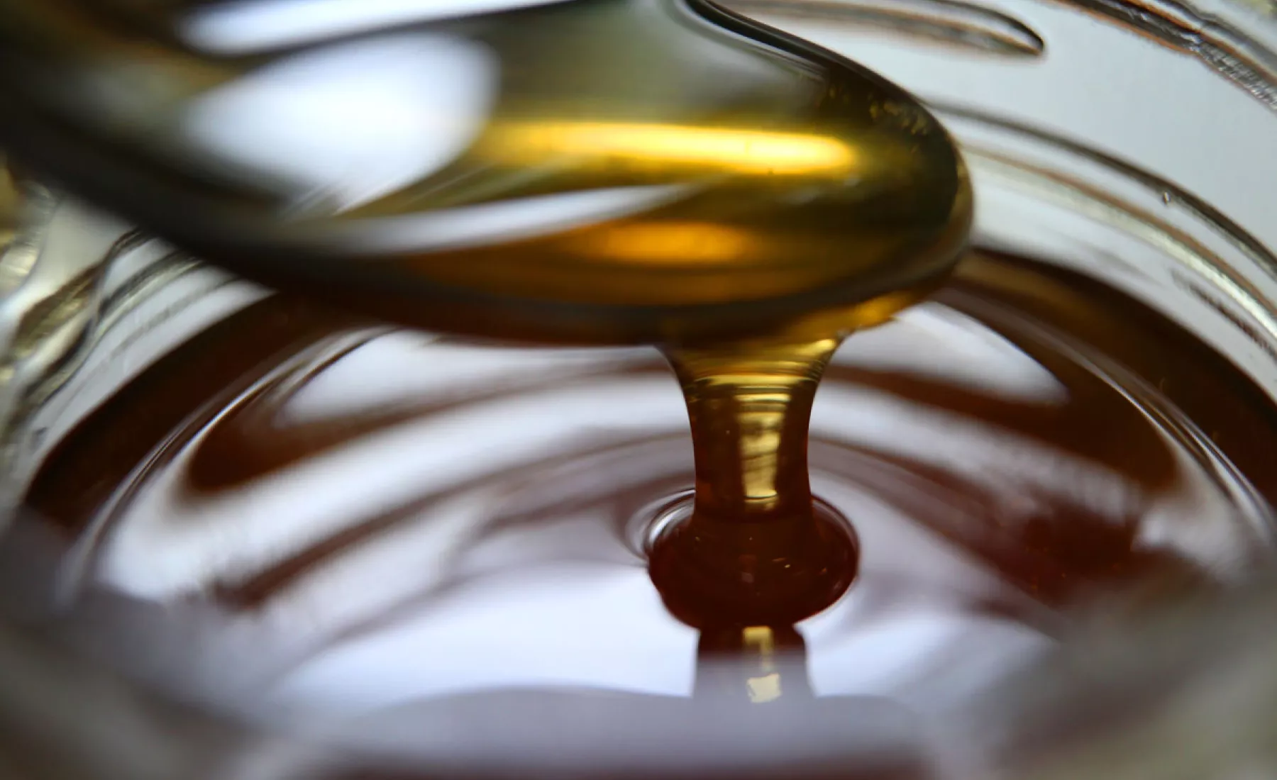 Honig fließt von einem Löffel in ein Honigglas.