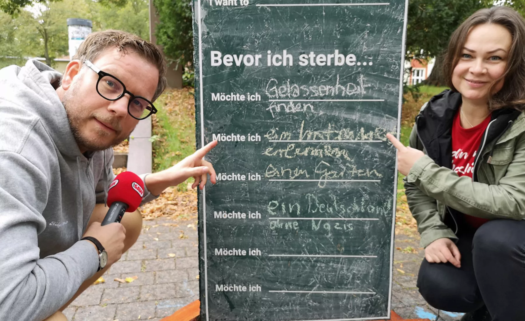 Holger Tapper und Nadine Rathke hocken vor einer Tafel-Stele im Nordpark Magdeburg