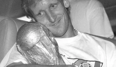 ARCHIV - 09.07.1990, Hessen, Frankfurt/Main: Andreas Brehme (l), damaliger deutscher Fußballnationalspieler, nimmt den WM-Pokal in den Arm