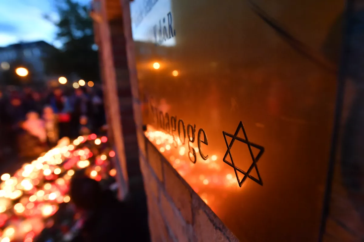 Menschen legen an der Mauer der Synagoge Blumen und Kerzen nieder.