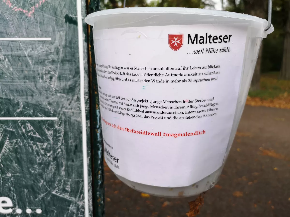 Eine Plastikeimer gefüllt mit Kreidestiften hängt an der Wunschstele im Nordpark in Magdeburg