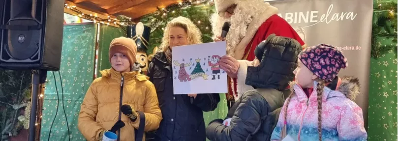 Weihnachtsmann zeigt ein von einem Kind gemaltes Weihnachtsbild
