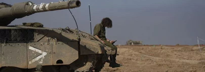 Ein israelischer Soldat sitzt auf einem Panzer und schaut auf ein Smartphone